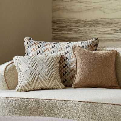 Multi color tan and brown pillows on a tan couch using designer fabrics